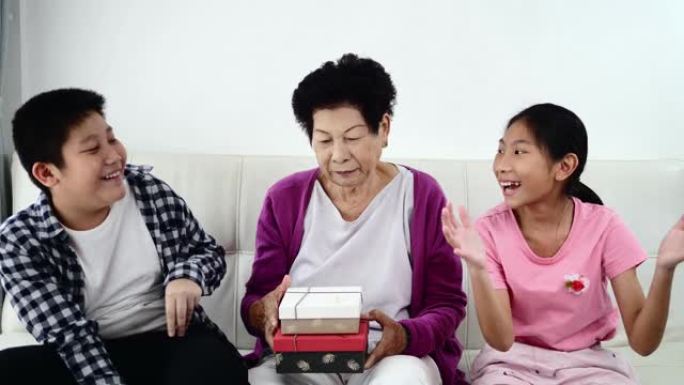亚洲高级妇女和她的孙子们拿着礼品盒，坐在家里的沙发上，度假概念。