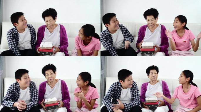 亚洲高级妇女和她的孙子们拿着礼品盒，坐在家里的沙发上，度假概念。