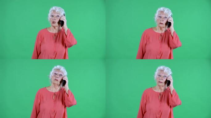 肖像老年妇女看着相机，用智能手机聊天。工作室绿色屏幕上穿着红色上衣的白发祖母。特写