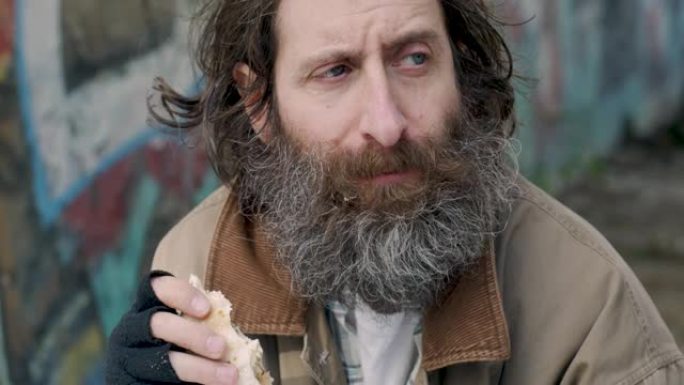 一个留着胡子的男人坐在外面吃着食物，满足了自己的饥饿