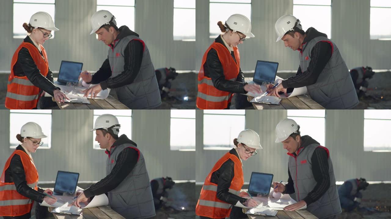 戴着防护头盔的工程师在焊接火花的背景下，根据机库中的图纸讨论新建筑物