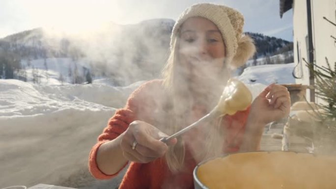 快乐的年轻女子在瑞士吃奶酪火锅，在冬季假期享受阿尔卑斯山和白雪皑皑的山脉。人们饮食传统当地观念