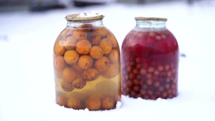 在街上的雪中关闭带有水果和浆果的罐装果汁。冬季在花园里密封的蜜饯罐