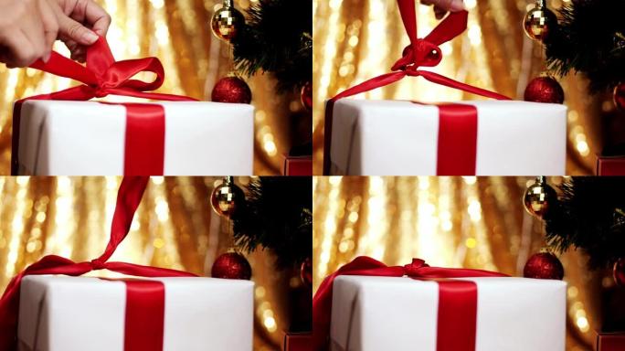 将红丝带放在带有圣诞灯背景的礼品盒上。