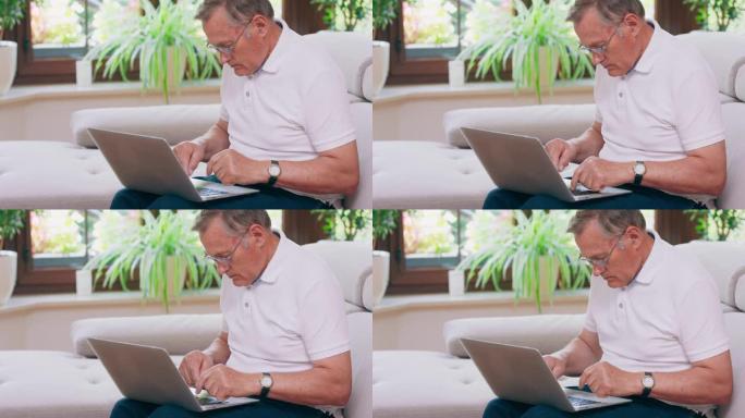 一名高级退休男子在家中沙发上的笔记本电脑上打字