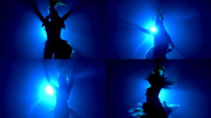 穿着羽毛制成的狂欢节服装的跳舞女人的仰视图。蓝色光线中苗条性感身材的轮廓。慢动作特写