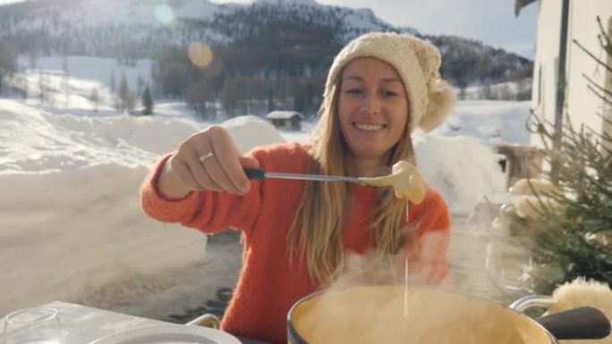 快乐的年轻女子在瑞士吃奶酪火锅，在冬季假期享受阿尔卑斯山和白雪皑皑的山脉。人们饮食传统当地观念