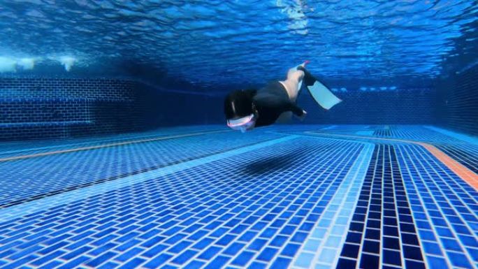 水下视图多莉女人穿一件长袖比基尼剪裁泳衣做动态呼吸暂停与双鳍鳍鳍在浅水池游泳