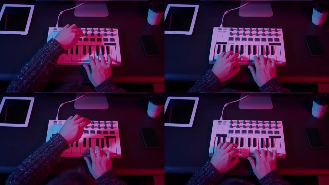 在带有霓虹灯的家庭工作室中使用midi键盘的手的俯视图