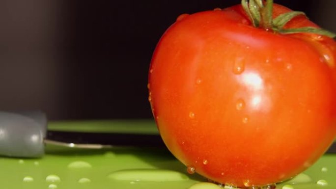 一个水滴成熟多汁的番茄躺在绿色板上，特写