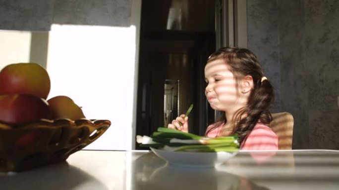 五岁的小女孩坐在餐桌上的厨房里，从盘子里取出苦涩健康的大葱，食欲大增。不寻常饮食习惯和健康素食的概念