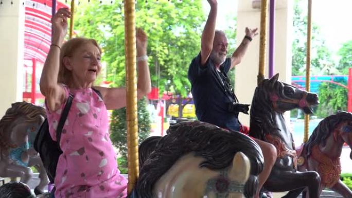 夏天，快乐的高级夫妇一起在户外游乐园骑旋转木马。疯狂的老男人和有趣的成熟女人在假期玩得开心