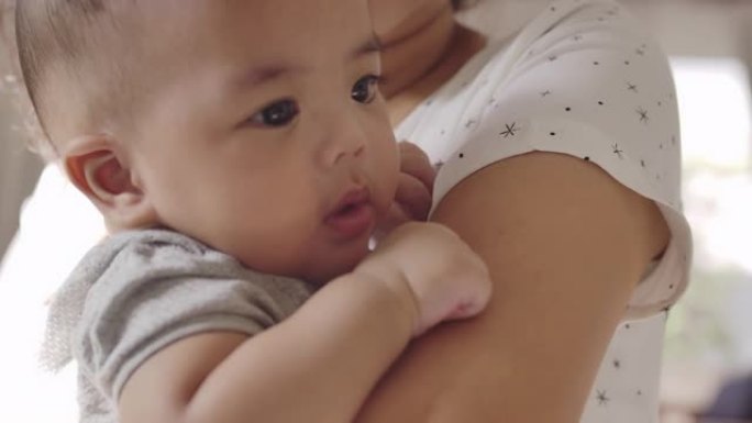 一个亚洲男婴和他年轻美丽的母亲抱着他在家里的客厅里温暖的爱和关怀。