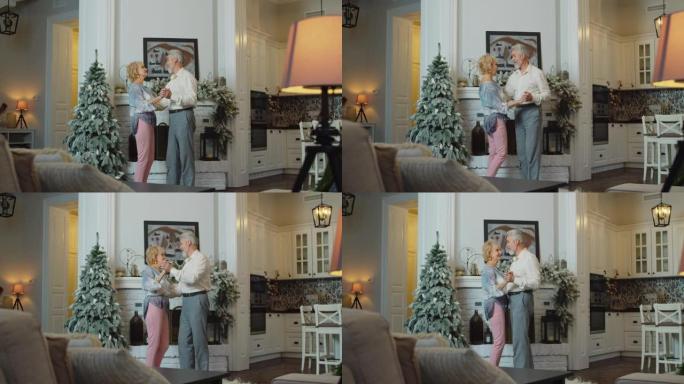 开朗的高级女子在装饰好的圣诞树前与丈夫跳舞，模仿唱歌。有趣的退休人员在除夕夜在家玩得开心。