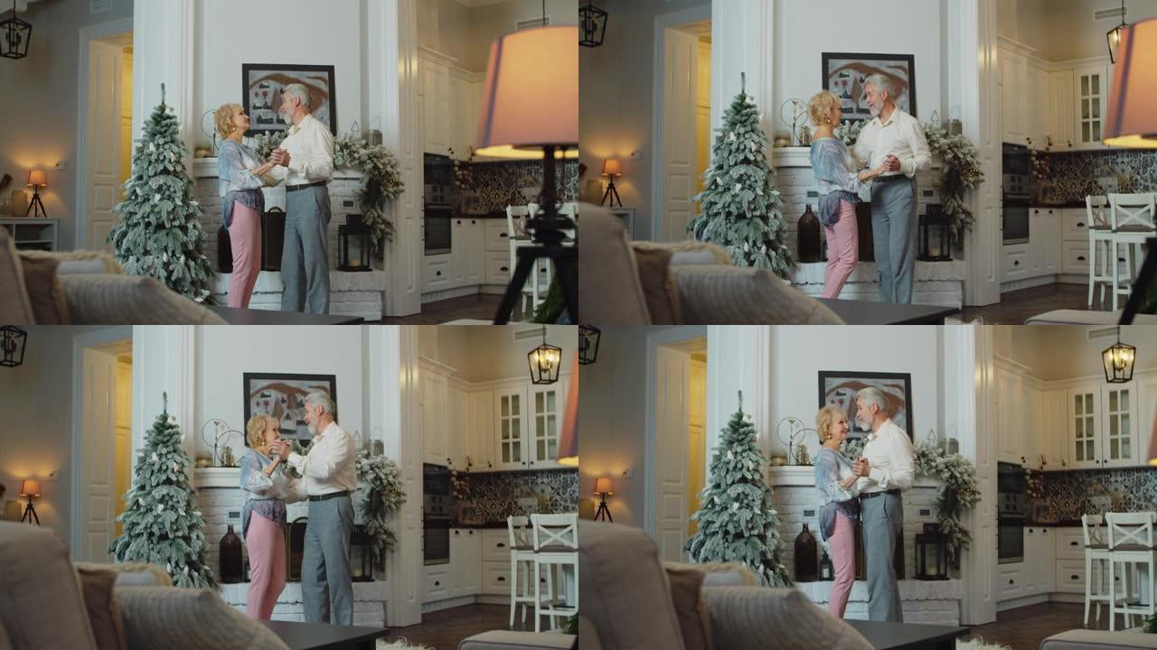开朗的高级女子在装饰好的圣诞树前与丈夫跳舞，模仿唱歌。有趣的退休人员在除夕夜在家玩得开心。
