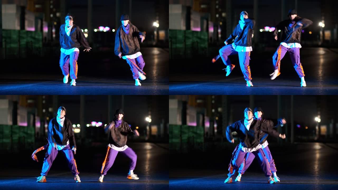 两个精力充沛的年轻女子在灯笼的灯光下，晚上在城市街道上跳着嘻哈，自由式跳舞。
