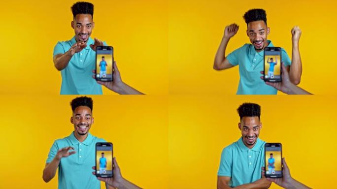 微笑的视频记录器非洲男子在黄色背景的智能手机摄像头前录制自己跳舞的视频。有影响力的人制作有趣的社交媒