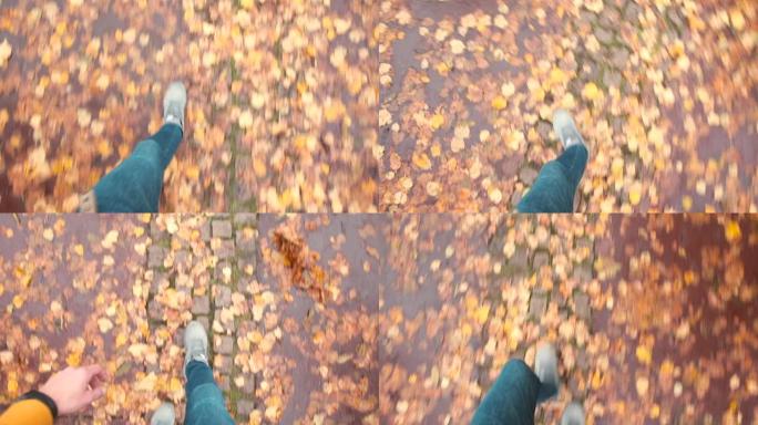 男人在秋天的树叶中沿着人行道行走，用脚迈出脚步。