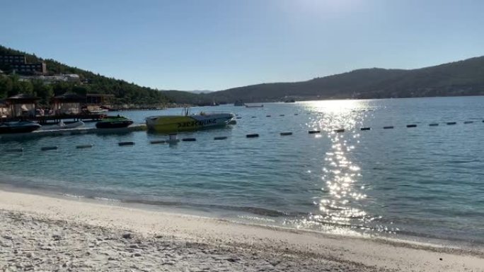 土耳其Lujo豪华酒店的4k翡翠泻湖在白色海滩上俯瞰常绿山丘，雪白的生态游艇，日光浴躺椅和竹伞