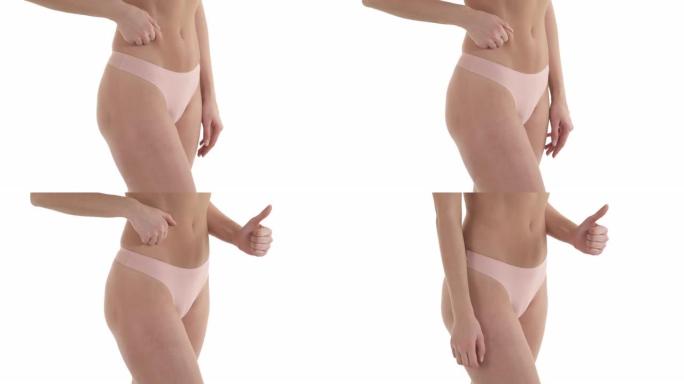 穿着内裤的苗条白人女性的中段展示了平坦腹部减肥的完美效果，并竖起了大拇指。孤立在白色背景上。