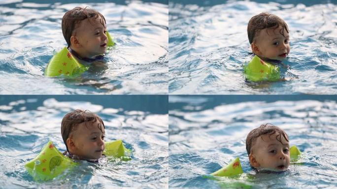 学步的男孩学习游泳，婴儿戴着手臂漂浮物