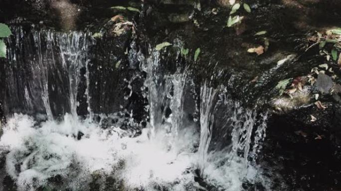 瀑布很小，瀑布流过石头，特写，森林里的一条小溪，水倾泻在自然界的石头上。
