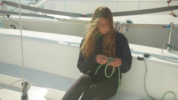 坐在运动游艇上，一个漂亮的女孩在帆船上的河流帆船赛前解开绳子