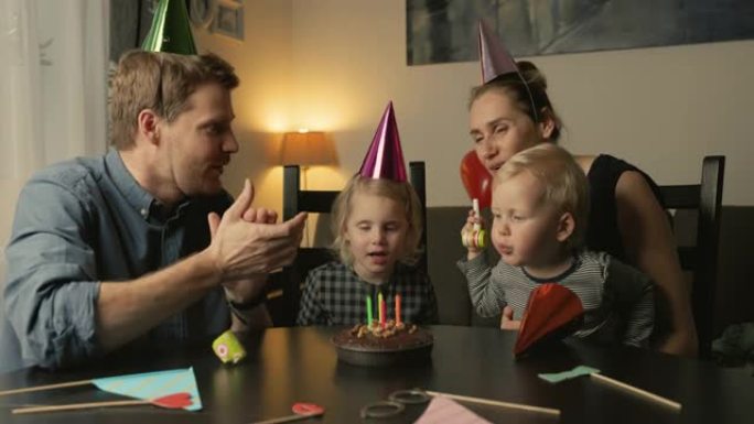 年轻幸福的家庭在家庆祝女儿生日。吹灭蛋糕上的蜡烛