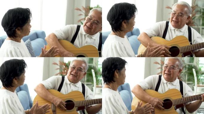 亚洲高级夫妇坐在沙发上，一起弹吉他。快乐微笑的老妇人拍手，而70多岁的吉他手丈夫唱歌。在家享受退休生