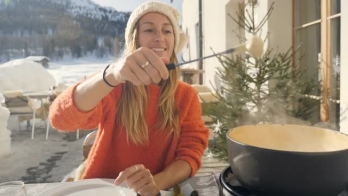 快乐的年轻女子在瑞士吃奶酪火锅，冬天享受阿尔卑斯山和白雪皑皑的山脉