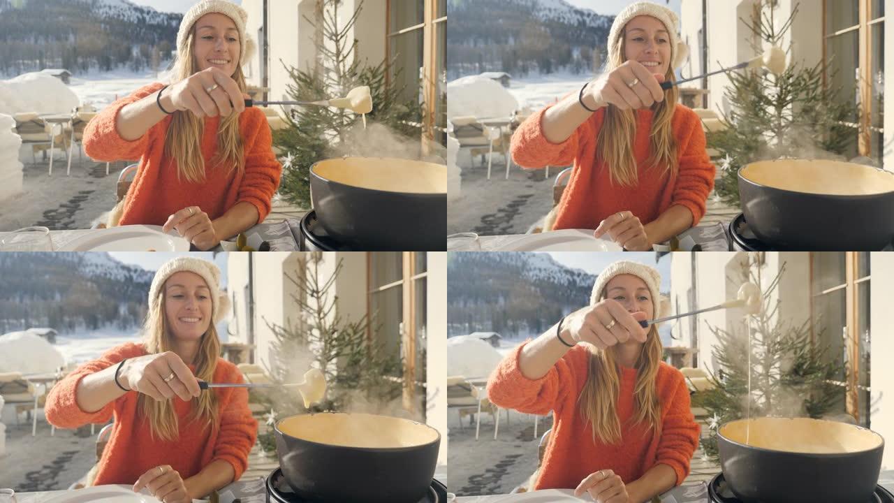 快乐的年轻女子在瑞士吃奶酪火锅，冬天享受阿尔卑斯山和白雪皑皑的山脉