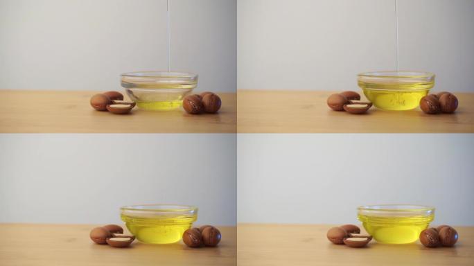 将摩洛哥坚果油倒入带有白色背景上的摩洛哥坚果籽的玻璃碗中。基于摩洛哥坚果油的化妆品概念。