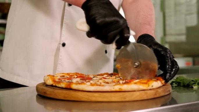 厨师在餐厅厨房用圆刀切披萨的特写镜头。