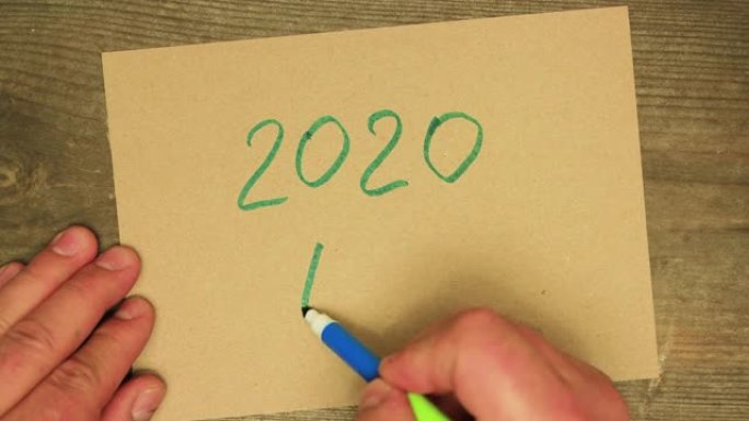 一只男性的手用蓝色毡尖笔在纸板上写下2020。