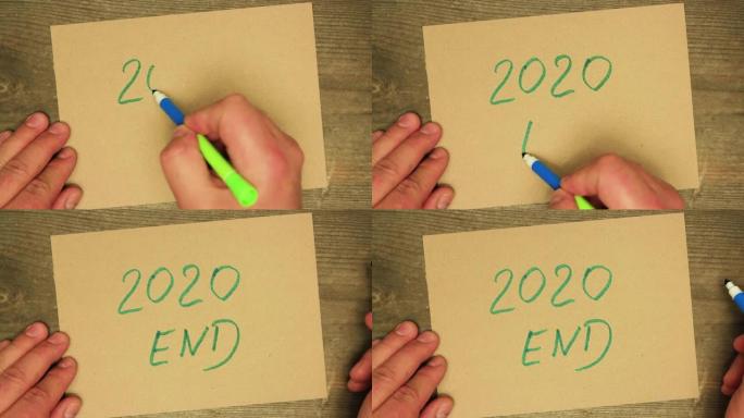 一只男性的手用蓝色毡尖笔在纸板上写下2020。