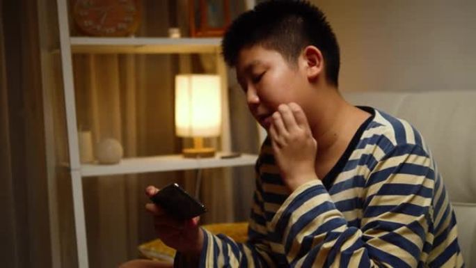 快乐的亚洲男孩在家坐在沙发上玩手机网络游戏，生活方式理念。