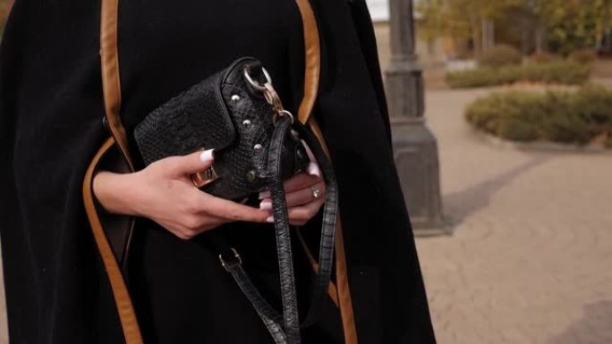 一个穿着斗篷的年轻女子在公园里拿着一个黑色钱包的特写镜头。