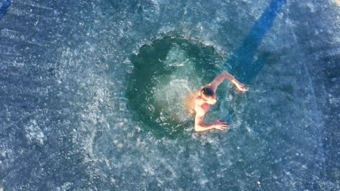 冬季游泳。年轻人在阳光明媚的日子跳入冬湖，背景是森林。多摄像机场景。摄像机2。空中，自上而下的视图