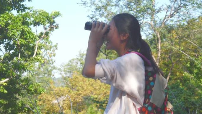 亚洲背包客女孩在与家人度假时使用具有自然背景的双筒望远镜。