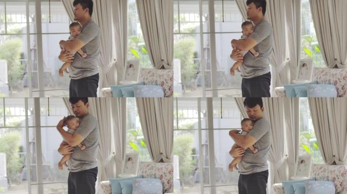 一位亚洲年轻的父亲坐在家里的客厅里，背着孩子，做运动，和他的男婴玩耍