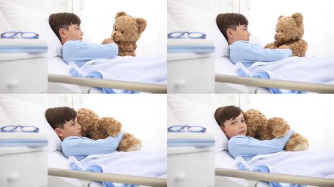 医院里的孩子独自躺在床上玩泰迪熊拥抱他并在镜头前微笑