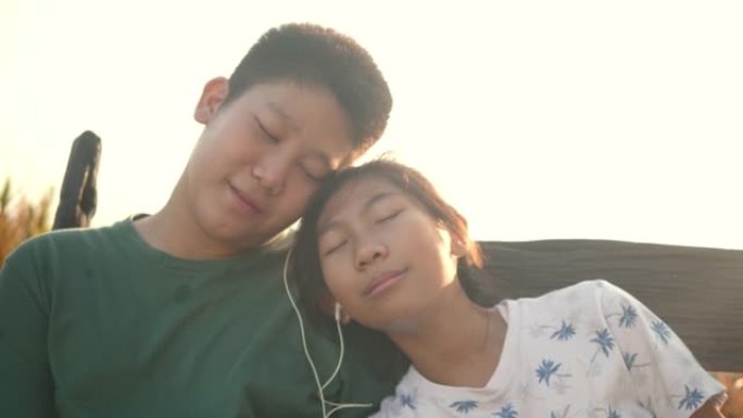 快乐的亚洲男孩为他的妹妹分享耳塞，并与太阳光背景，技术概念一起听歌。