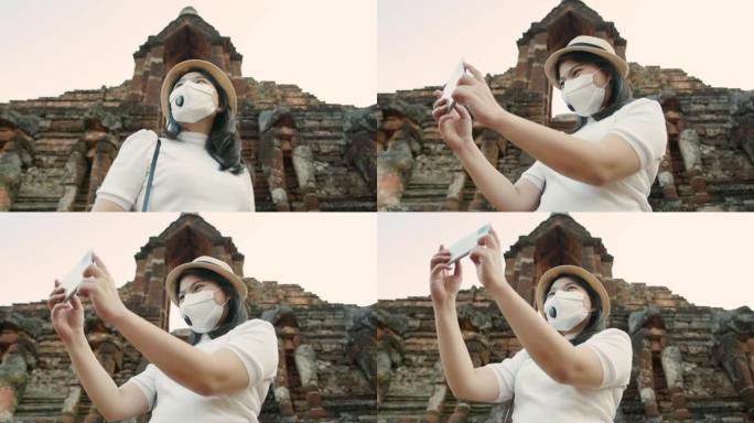 社交距离安全旅行新的正常生活方式亚洲女性戴着防护口罩步行拍照与智能手机旅游泰国古亚神庙日落时刻