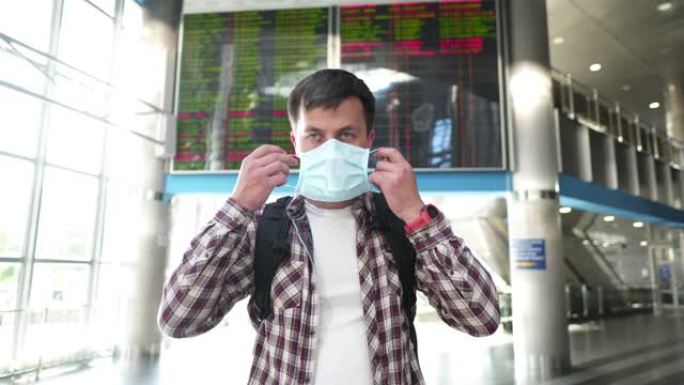 关于旅行时在公共场所戴防护口罩的重要性的社交视频。男子戴上面具，站在机场航站楼背景时间表板上显示竖起
