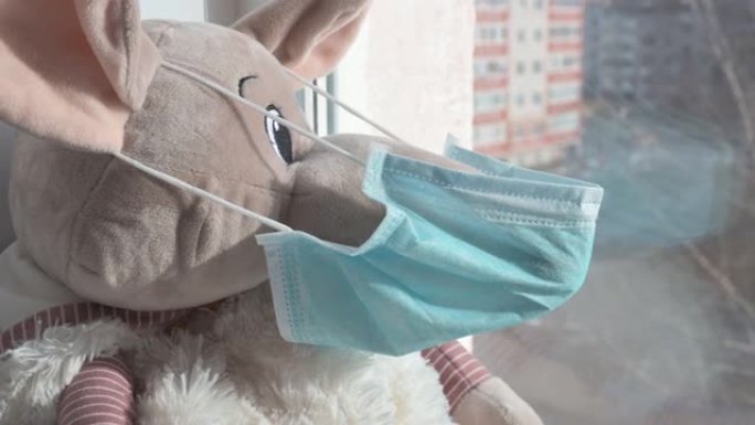 戴着医用防护面具的玩具鼠坐在窗台上