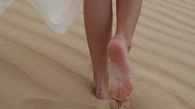 一个穿着白色连衣裙的赤脚黑发女人沿着沙漠沙滩行走。慢动作。