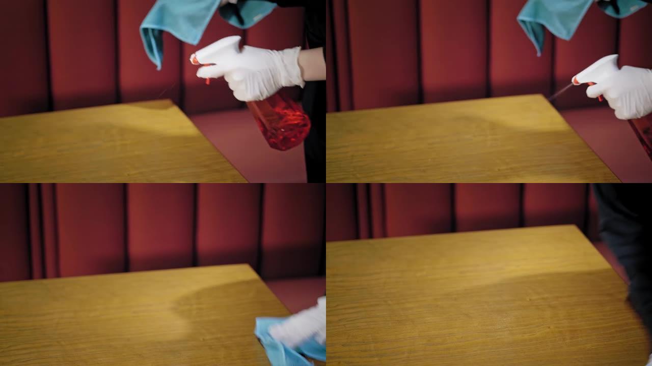 特写镜头，服务员戴着防护手套，用防腐喷雾剂和清洁巾擦拭餐厅的桌子。大流行冠状病毒
