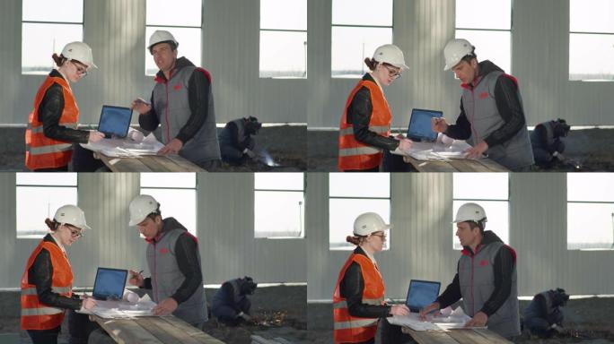 戴着防护头盔的建筑工程师男人和女人根据机库中的图纸讨论新建筑物焊接火花的背景