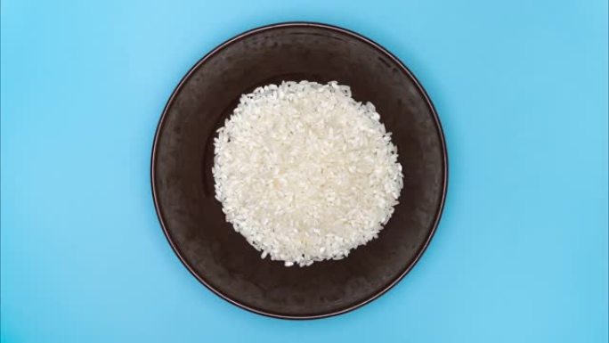 白米饭装满桌子上的棕色盘子。俯视图，停止运动。