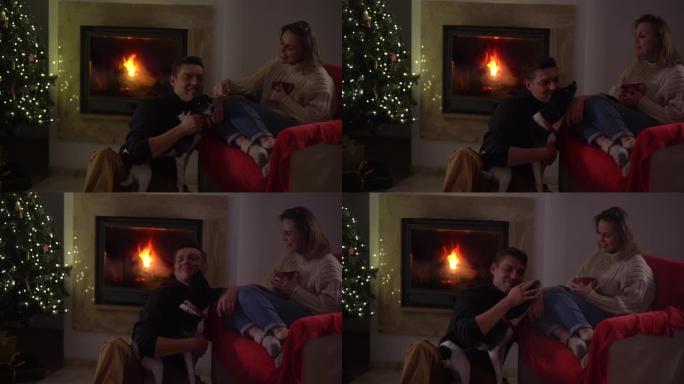 丈夫和妻子，幸福的夫妇与狗在舒适温暖的家庭服装的背景装饰。一个坐在地板上的男人在打电话。圣诞树和舒适